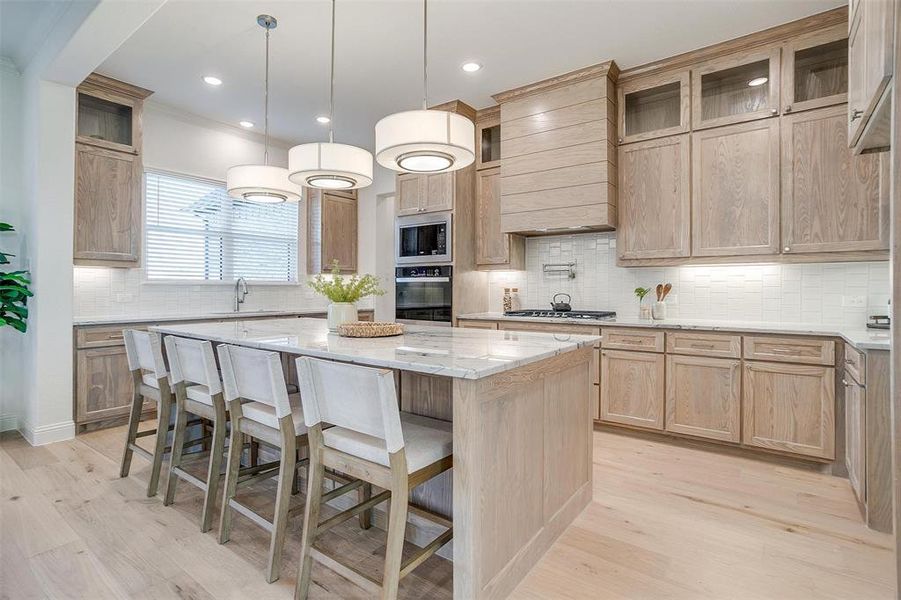 Kitchen featuring Quartzite countertops, tasteful backsplash, light hardwood / wood-style flooring, a kitchen island, and appliances with stainless steel finishes