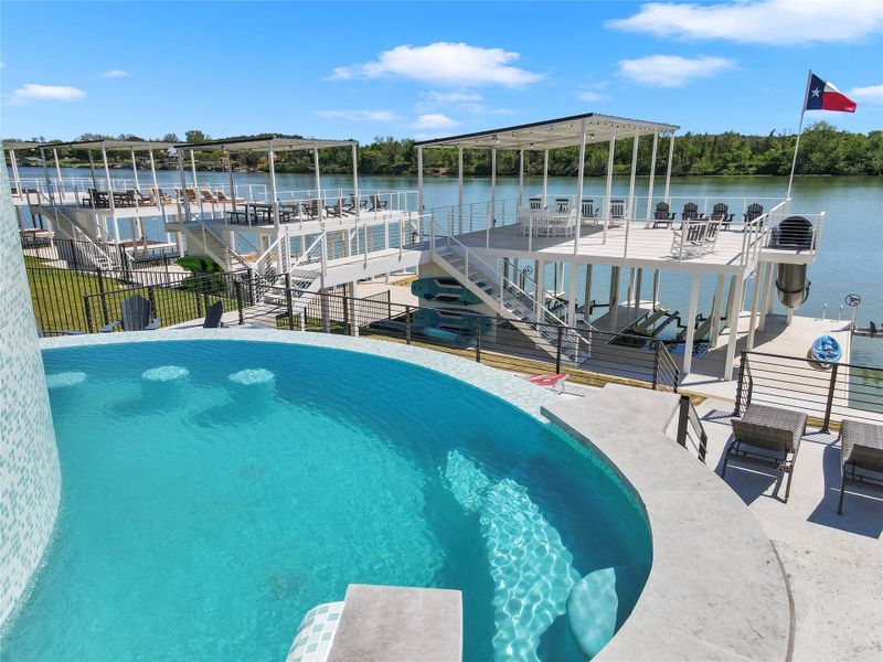 An elevated sparkling pool overlooks multi-level boat docks along the scenic waterfront.