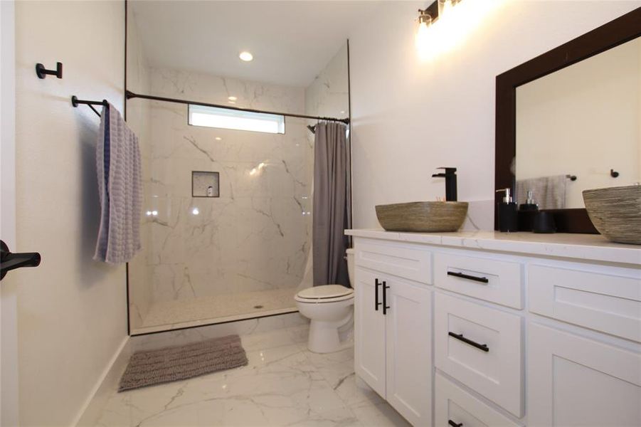 Full bath with a marble finish shower, double vanity, and light marble finish floors Full bath with a marble finish shower, double vanity, and light marble finish floors
