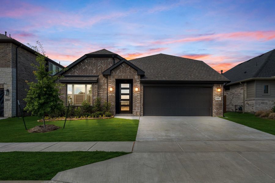 Single-story brick home with two-car garage, modern front door, and green lawn at dusk