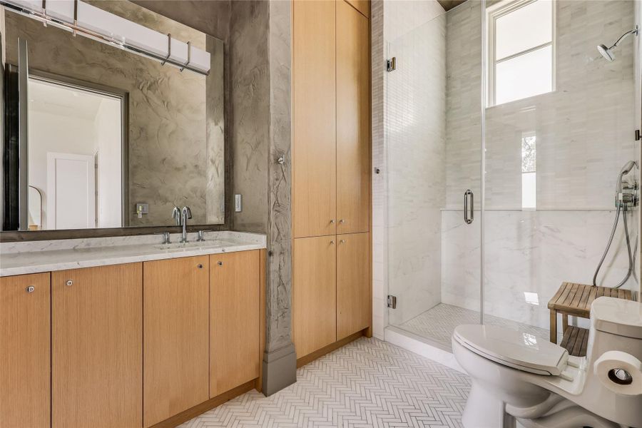 Herringbone tile flooring and a glass-enclosed shower create a bright and clean bathroom.