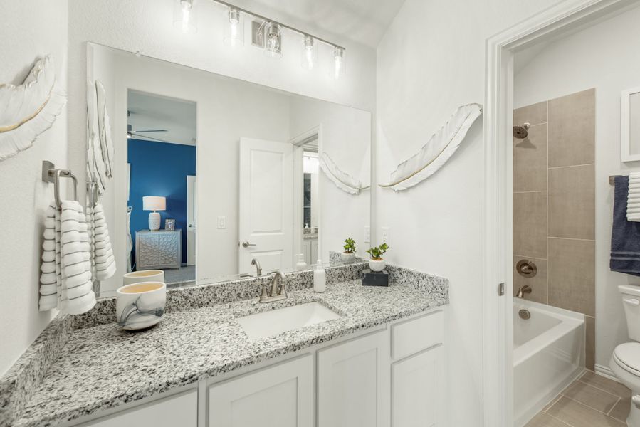 Bathroom with granite countertop, white cabinets, large mirror, and tiled tub-shower combo