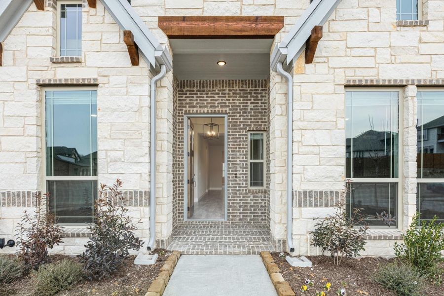 Home entrance with brick and stone exterior, wood beam porch cover, and open front door with pendant light Home entrance with brick and stone exterior, wood beam porch cover, and open front door with pendant light