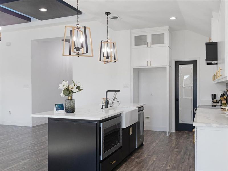 Kitchen featuring vaulted ceiling, white cabinetry, hanging light fixtures, and stainless steel appliances