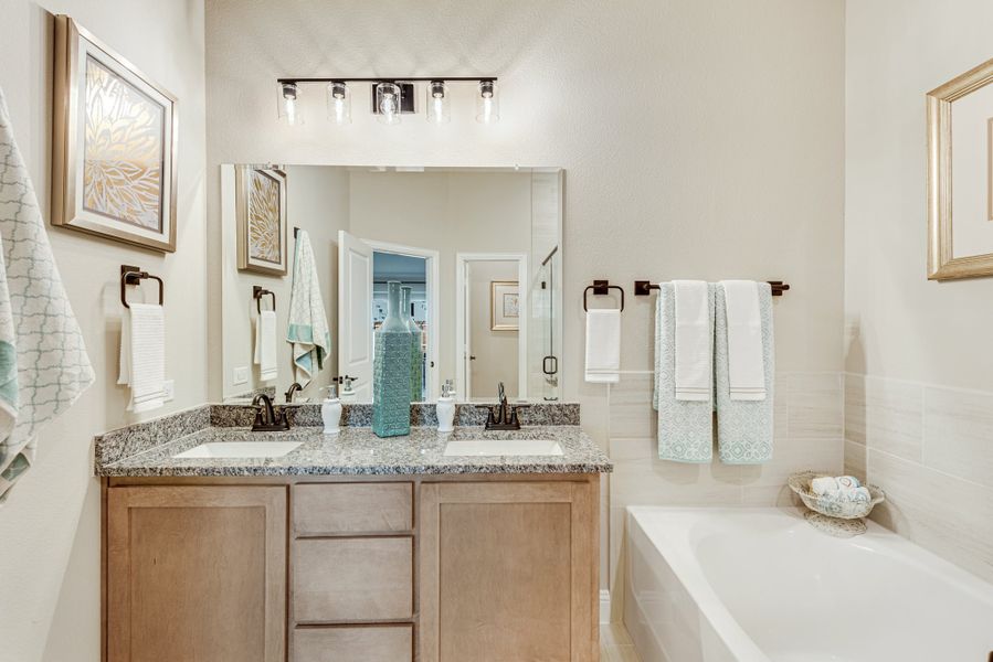 Bathroom with double sink vanity, granite countertop, wood cabinets, and soaking tub beside large mirror