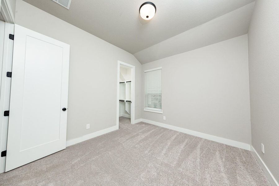 This secondary bedroom features a sloped ceiling, plush carpet flooring, a large window, a walk-in closet, and an ensuite secondary bathroom. This secondary bedroom features a sloped ceiling, plush carpet flooring, a large window, a walk-in closet, and an ensuite secondary bathroom.