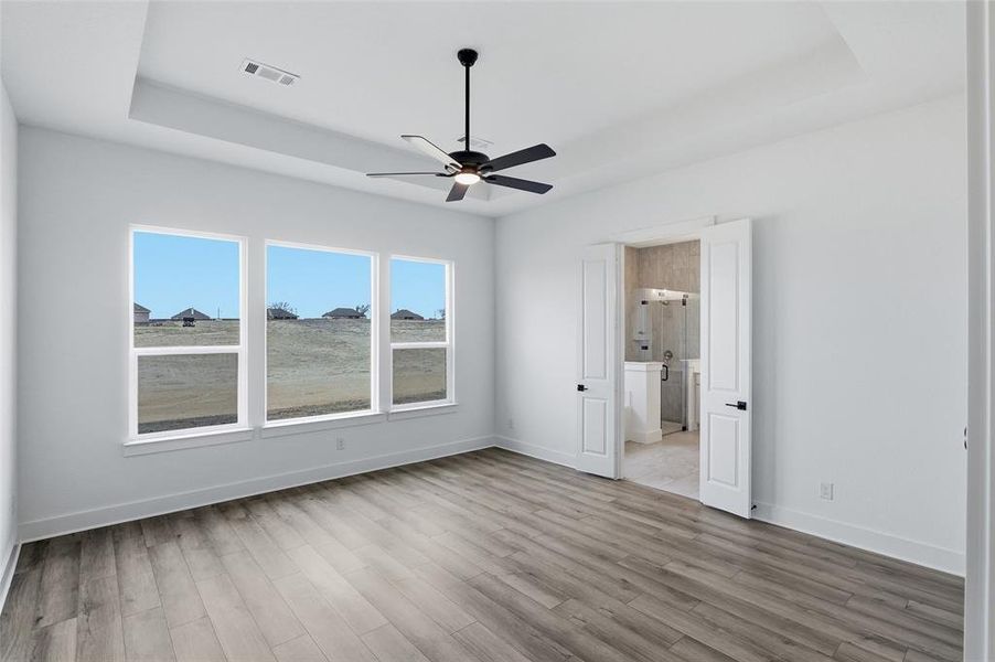 Unfurnished bedroom with a raised ceiling, ceiling fan, light wood-style floors, and connected bathroom