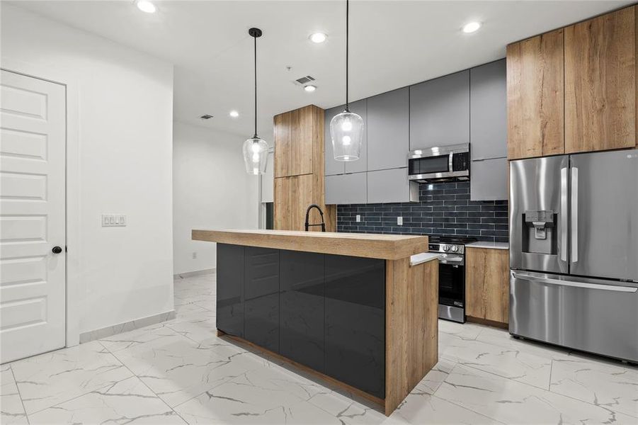 Kitchen featuring light marble finish floors, appliances with stainless steel finishes, modern cabinets, light countertops, and backsplash