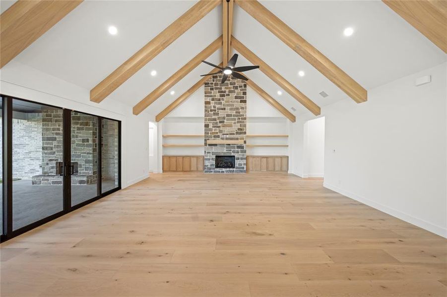 Spacious room featuring vaulted ceilings with exposed wood beams, a stone fireplace, wood-finish flooring, and recessed lighting