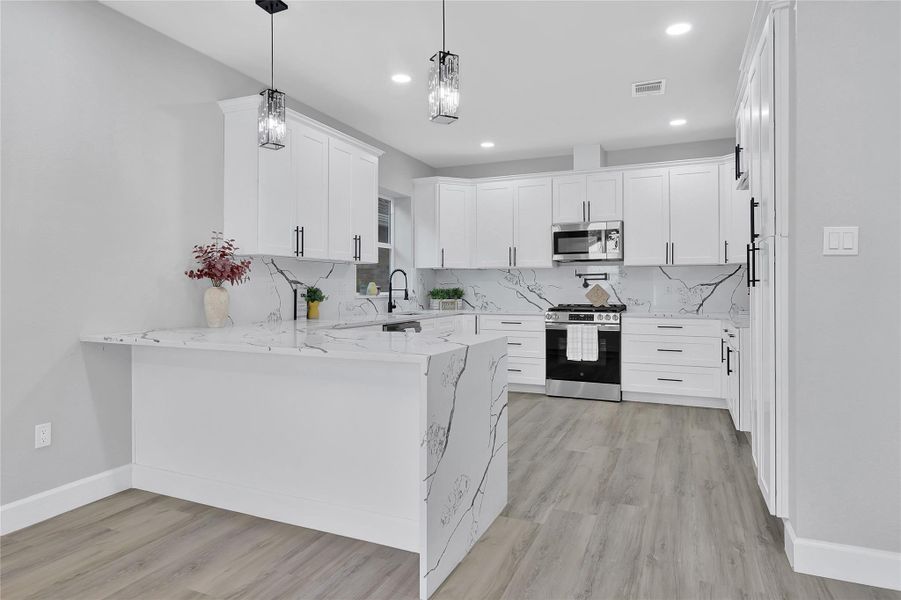 Modern kitchen with sleek white cabinetry, marble-patterned countertops, and backsplash. Features stainless steel appliances, pendant lighting, and wood-look flooring, creating a bright and elegant space.
