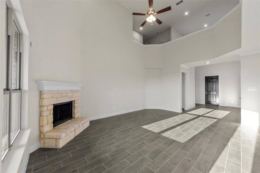 Unfurnished living room with a towering ceiling, a stone fireplace, a ceiling fan, wood tiled floors, and recessed lighting Unfurnished living room with a towering ceiling, a stone fireplace, a ceiling fan, wood tiled floors, and recessed lighting