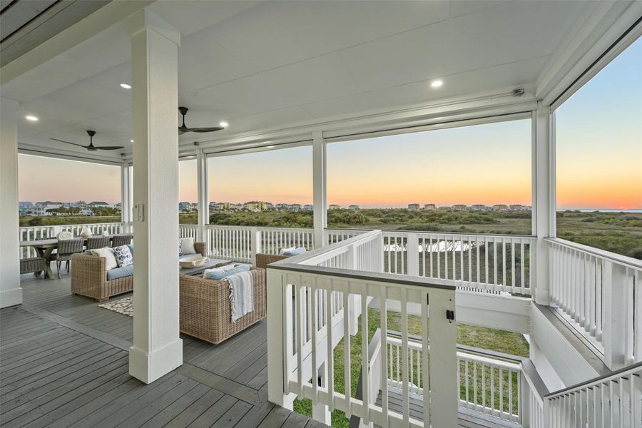 This photo showcases a spacious, 38' x 20' covered outdoor deck with comfortable seating and ceiling fans. It offers panoramic views of a serene landscape and the bay, perfect for enjoying sunsets.