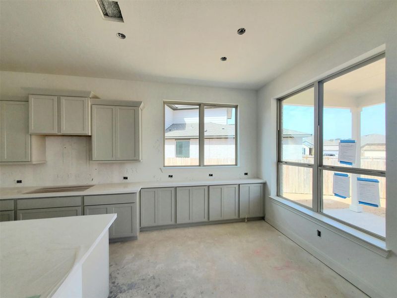 Kitchen with baseboards, light countertops, unfinished concrete flooring, and gray cabinetry