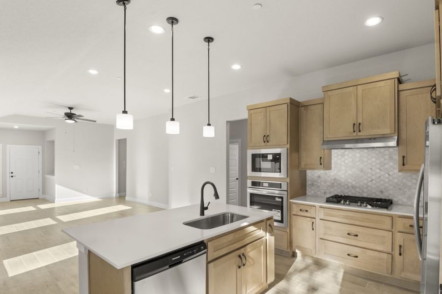 Image of a one story home kitchen with a white center island with a sink, light brown cabinets, marble backsplash, and stainless steel appliances Image of a one story home kitchen with a white center island with a sink, light brown cabinets, marble backsplash, and stainless steel appliances