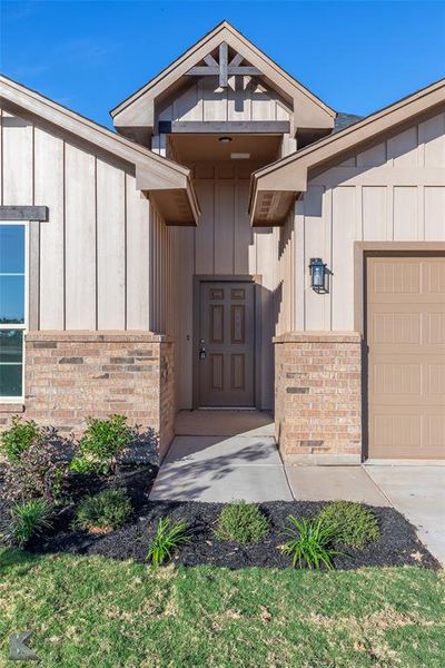 Doorway to property featuring board and batten siding, a garage, and brick.