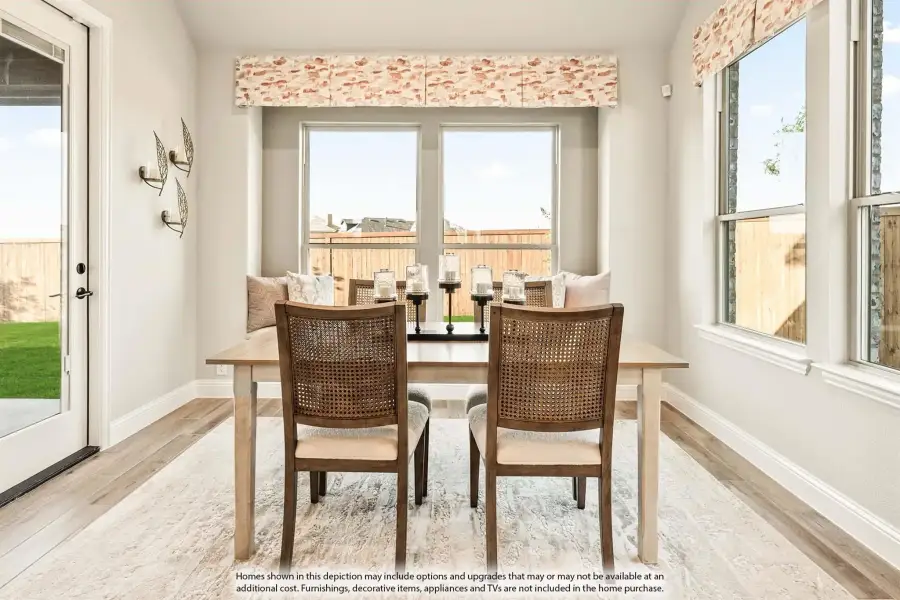 Bright dining nook with wood table, cane chairs, built-in bench seating, and large windows overlooking a fenced backyard.
