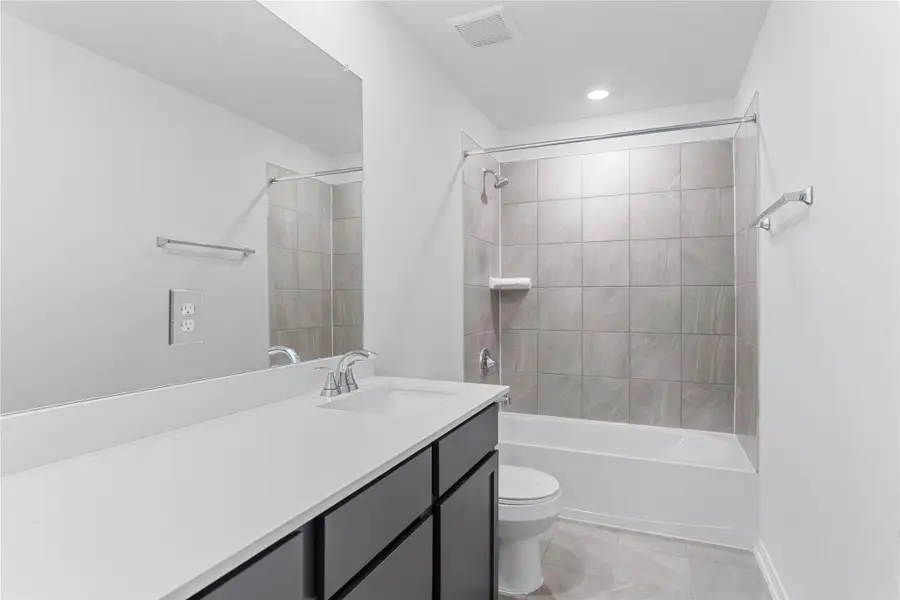 The secondary bathroom showcases tile flooring, a bath/shower combo with Daltile tile surround, a vanity with knee space and stunning light countertop, a mirror, sleek fixtures, and contemporary finishes throughout.