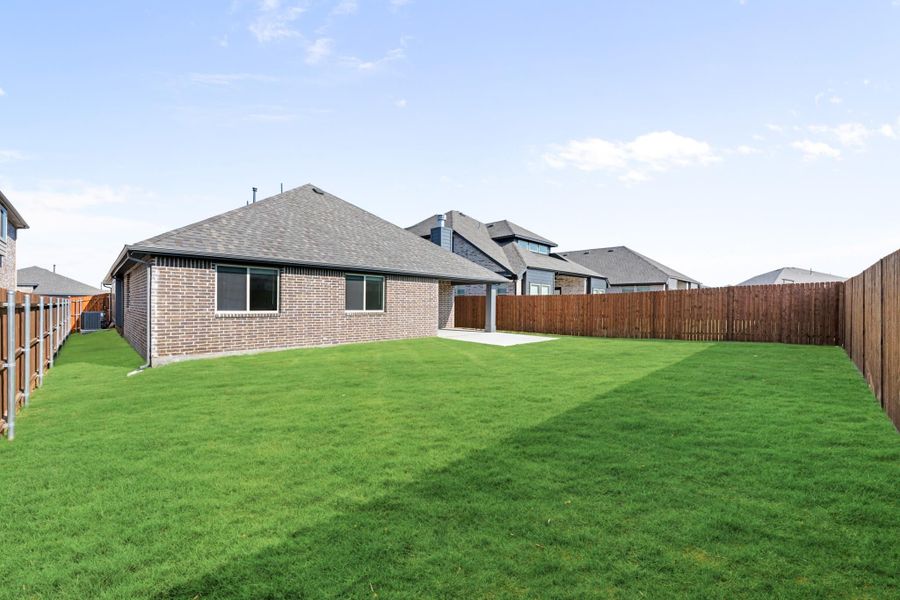 Backyard of brick home with large green lawn, covered patio, and wood privacy fence Backyard of brick home with large green lawn, covered patio, and wood privacy fence