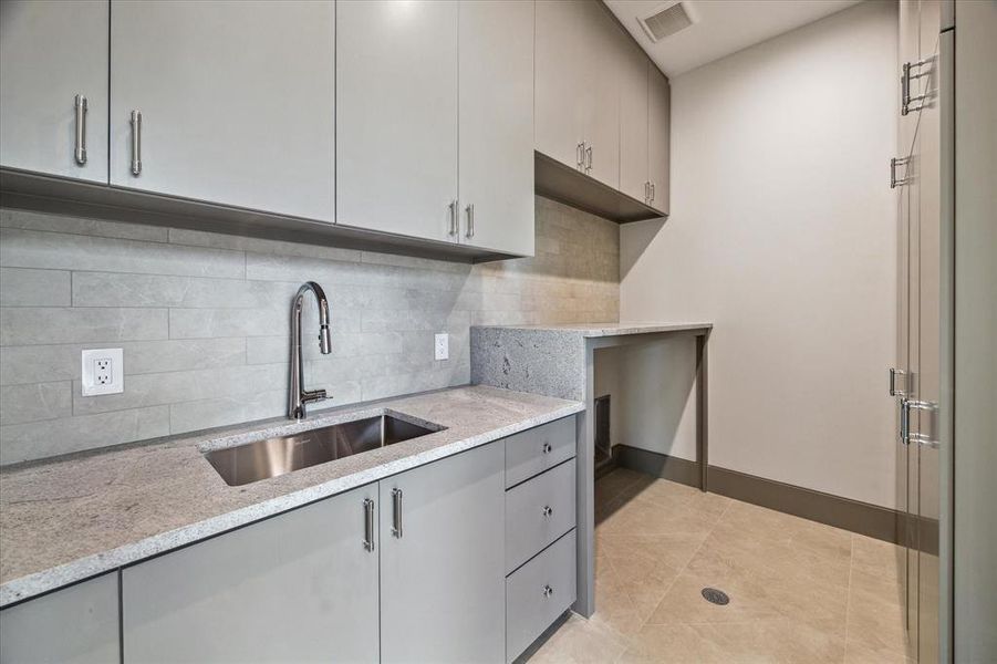 A utility room is conveniently located on each floor. The second-floor utility room is equipped with a PROFLO single hole pull-out spray kitchen faucet, an Elkay undermount single bowl kitchen sink, and a PROFLO drain strainer. It features Sterlina Ivory floor tile, Himalaya White countertops and backsplash, as well as washer and dryer connections for added functionality.