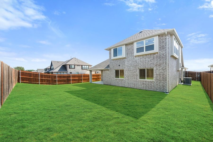 Two-story brick home with large grassy backyard enclosed by wood privacy fence