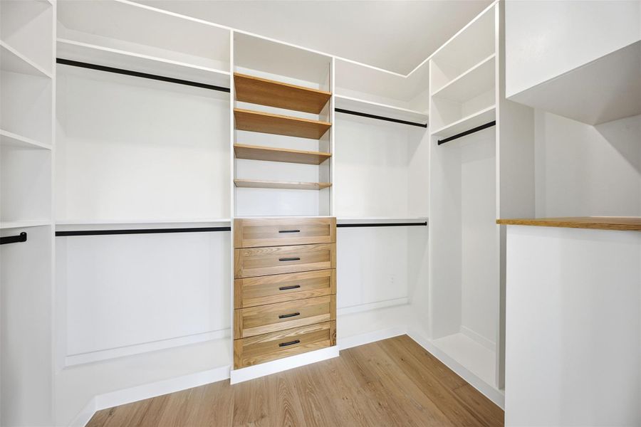 The custom walk-in closet offers a mix of hanging rods, open shelving, and a central dresser unit with wood-grain finishes.