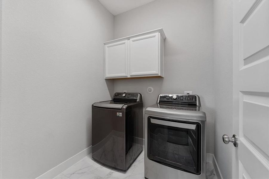 This walk in laundry room  with a storage cabinet above, all set against neutral walls and marble-like flooring.