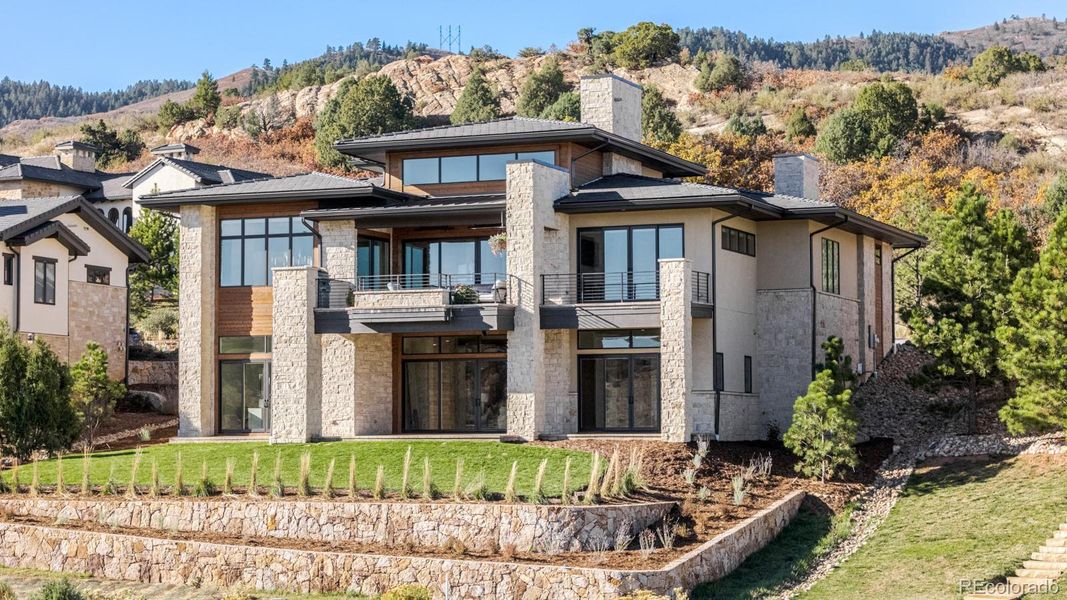 A newly designed back lawn offers an inviting expanse for recreation and gatherings, while terraced planting beds cascade gracefully toward the open space and golf course beyond.