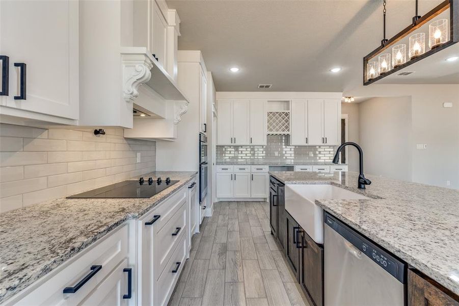 Kitchen with dishwasher, white cabinetry, light stone countertops, and pendant lighting