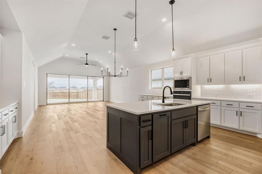 Kitchen with suspended lighting, tasteful backsplash, an island with sink, two tone color scheme, and light wood finished floors