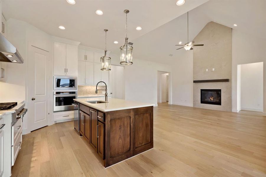 Kitchen with stainless steel appliances, pendant lighting, open floor plan, an island with sink, and light wood-style flooring