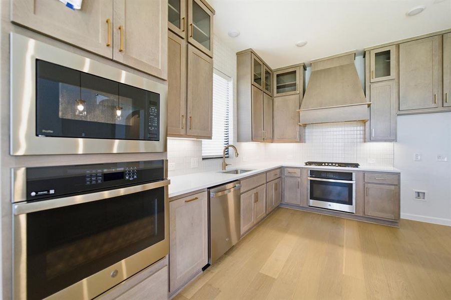 Modern kitchen featuring light wood-finish cabinetry with brass hardware, stainless steel appliances, white subway tile backsplash, and light wood-finish flooring Modern kitchen featuring light wood-finish cabinetry with brass hardware, stainless steel appliances, white subway tile backsplash, and light wood-finish flooring