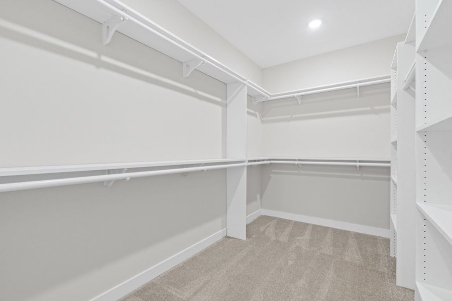 Built-in white shelving and hanging rods in a carpeted closet with recessed lighting Built-in white shelving and hanging rods in a carpeted closet with recessed lighting