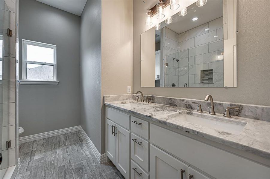 Bathroom with double sink vanity, toilet, a tile shower, and hardwood / wood-style flooring