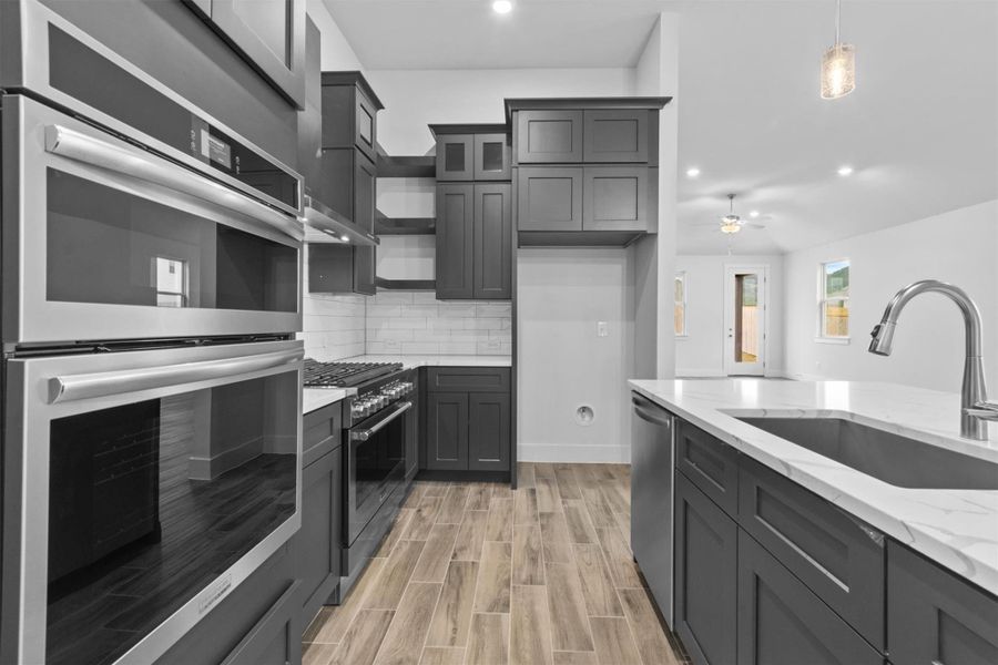 Kitchen featuring pendant lighting, appliances with stainless steel finishes, sink, backsplash, and light stone counters