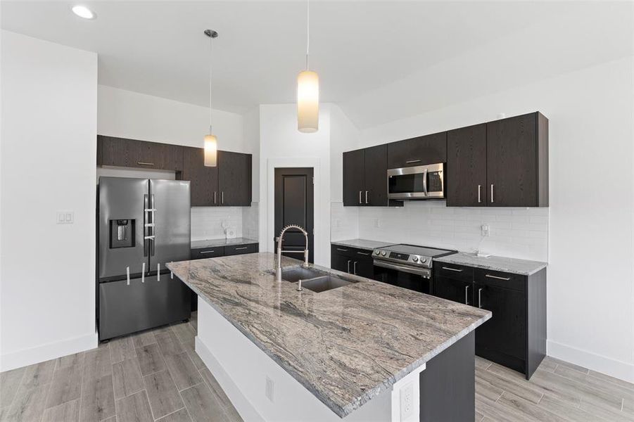 Kitchen with pendant lighting, sink, stainless steel appliances, and a kitchen island with sink