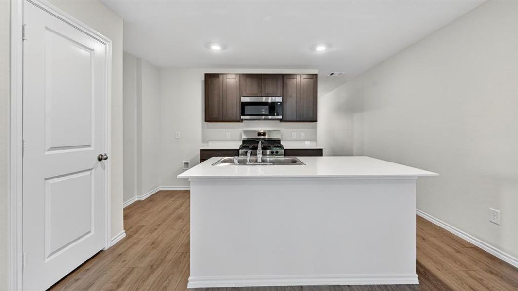 Kitchen featuring a white island with an undermount sink, dark wood-finish cabinetry, stainless steel appliances, and wood-finish flooring