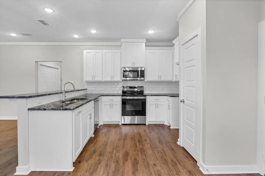 Kitchen with stainless steel appliances, a peninsula, a sink, decorative backsplash, and white cabinets