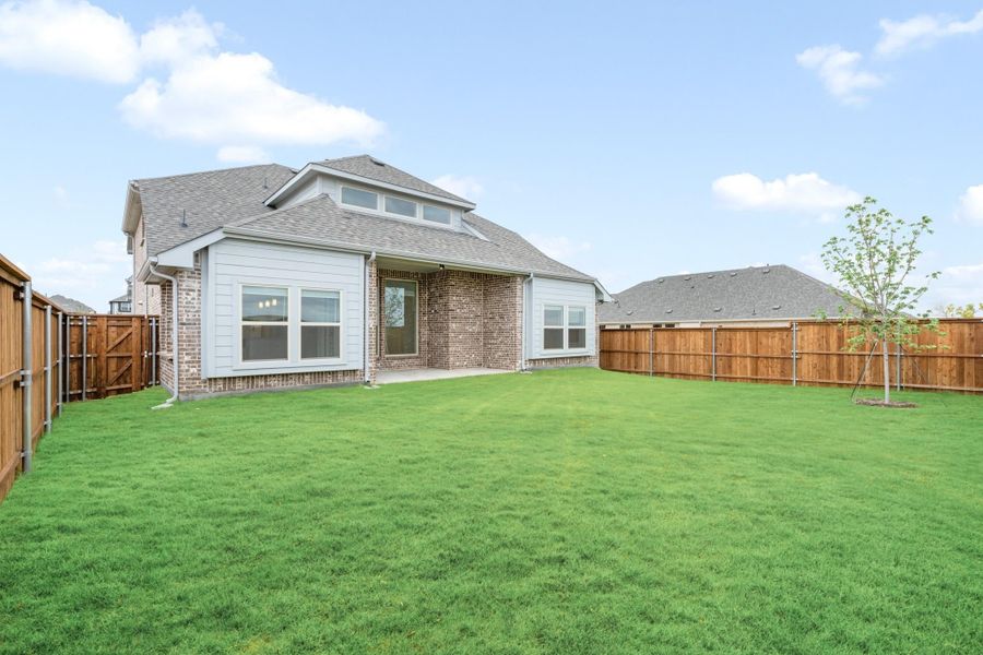 Rear view of brick and siding home with large fenced backyard, covered patio, and young tree