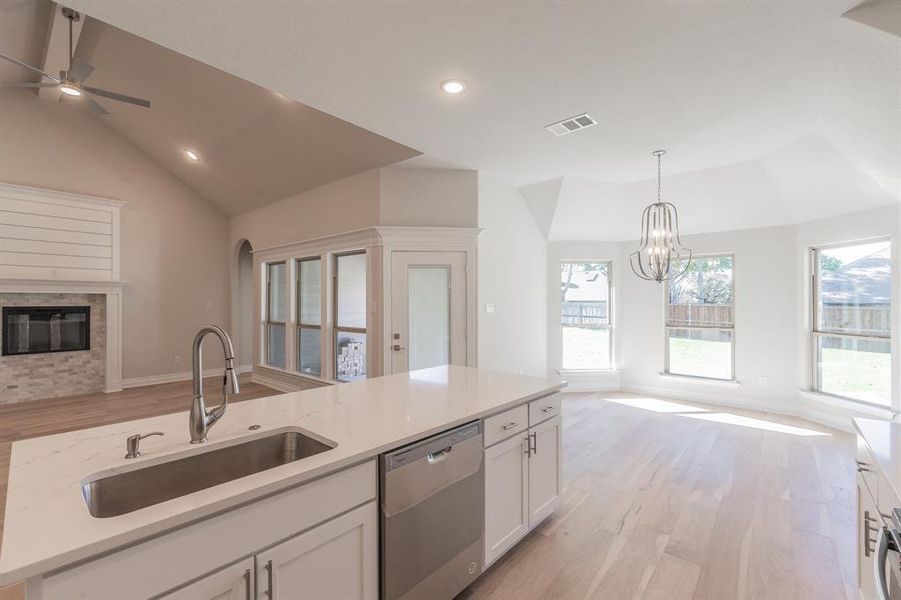 Kitchen with dishwasher, white cabinets, sink, light wood-type flooring, and light stone counters