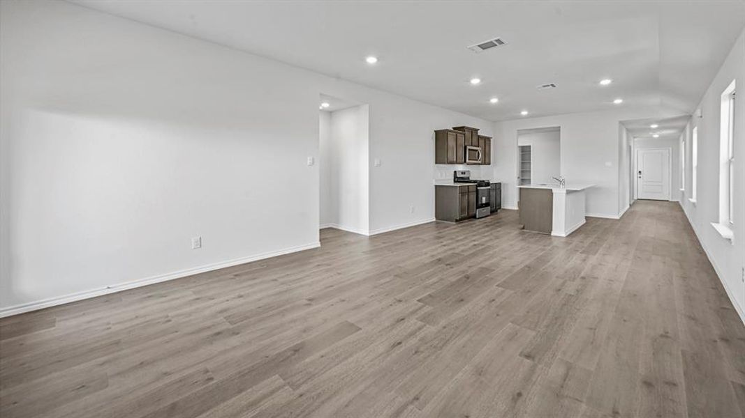 Expansive open-concept room featuring wood-finish flooring, recessed lighting, and a modern kitchen with dark cabinetry and stainless steel appliances