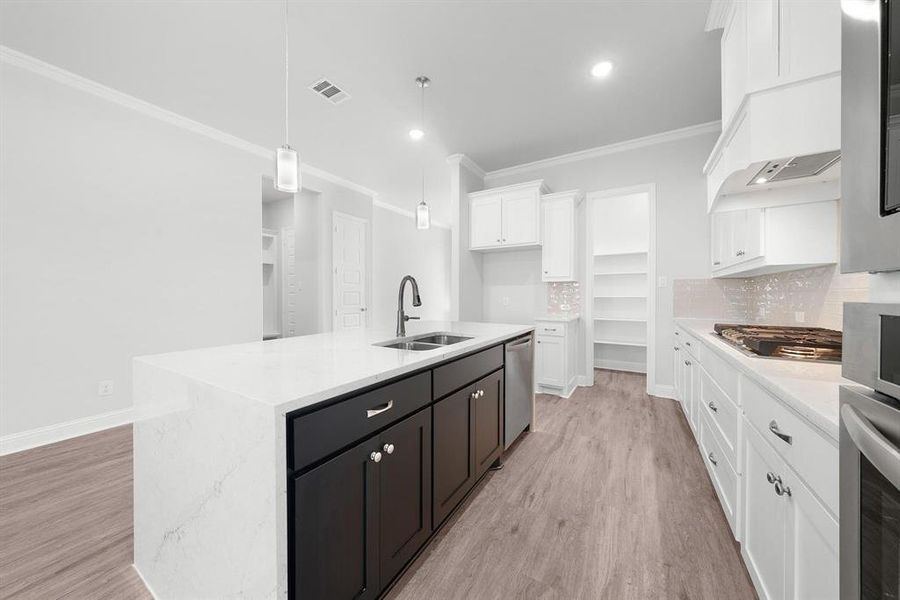 Kitchen featuring crown molding, island with granite countertops, white cabinets, luxury vinyl flooring, tile backsplash, large walk-in pantry, and pendulum light fixtures.