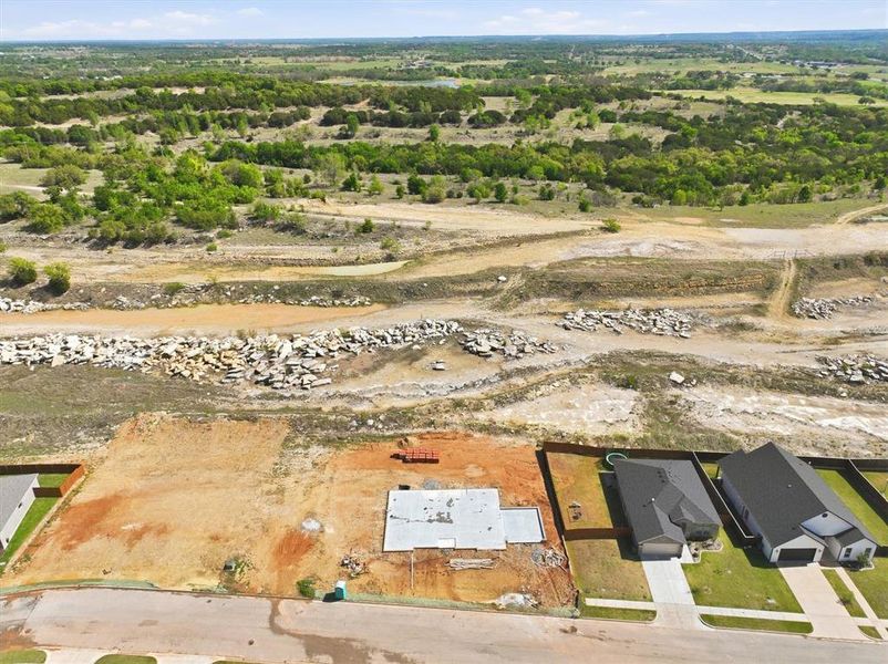 This aerial view showcases a property with a concrete foundation, positioned on a graded lot with an adjacent paved road This aerial view showcases a property with a concrete foundation, positioned on a graded lot with an adjacent paved road