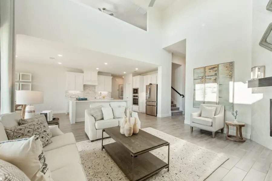 Open-concept living room with high ceilings flowing into white kitchen with stainless steel appliances and light wood floors