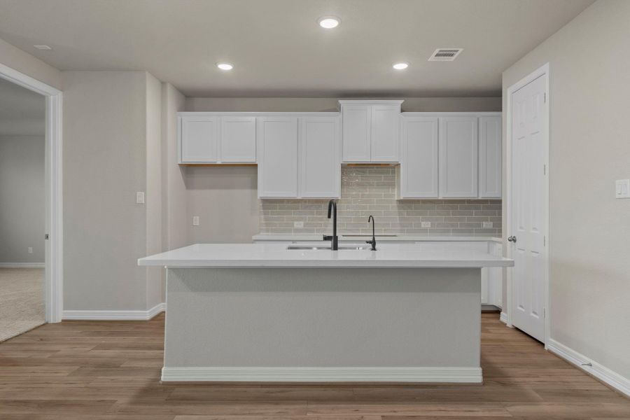 This light and bright kitchen features a large quartz island, white cabinets, a large sink overlooking your family room, recessed lighting, and beautiful backsplash. This light and bright kitchen features a large quartz island, white cabinets, a large sink overlooking your family room, recessed lighting, and beautiful backsplash.