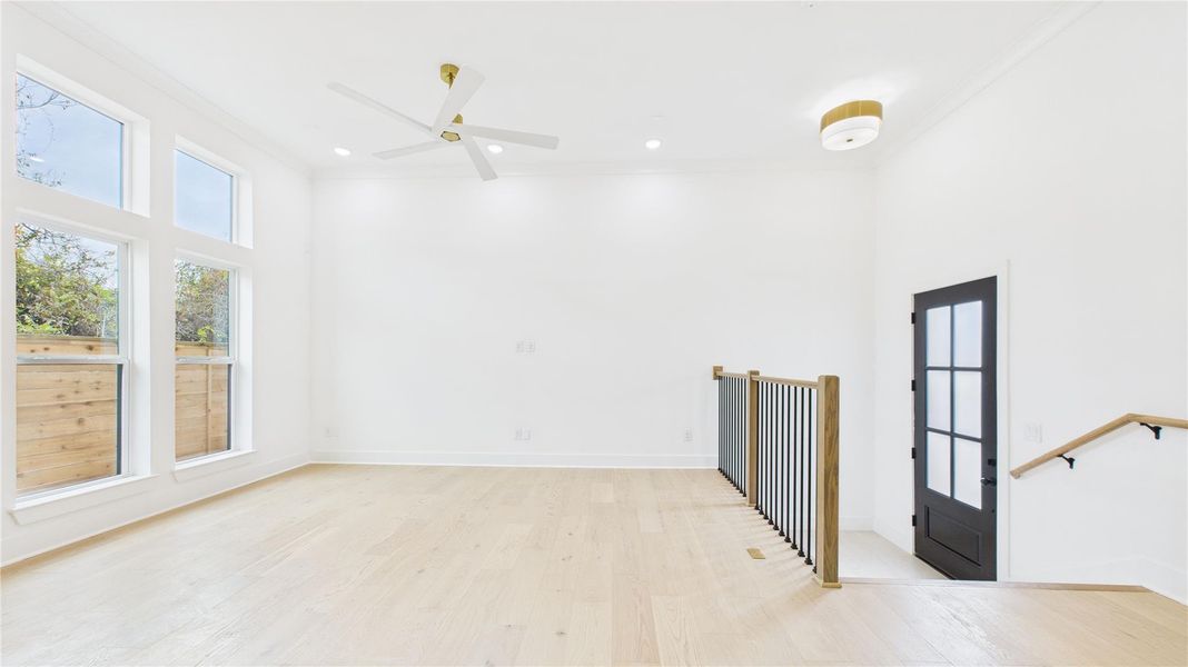 Bright, airy and open living space with high ceilings, large windows, and light wood floors. Features include a modern ceiling fan, sleek railing, and a stylish black and opaque glass paneled door. Perfect for a contemporary home aesthetic.