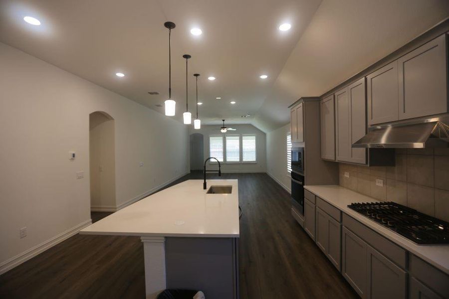 Open-concept kitchen featuring an island with a stainless steel sink, pendant lighting, built-in double ovens, a gas cooktop, and gray cabinetry