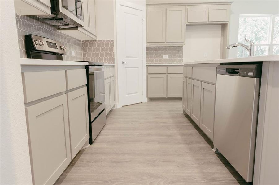 Kitchen featuring appliances with stainless steel finishes, light wood-type flooring, and backsplash