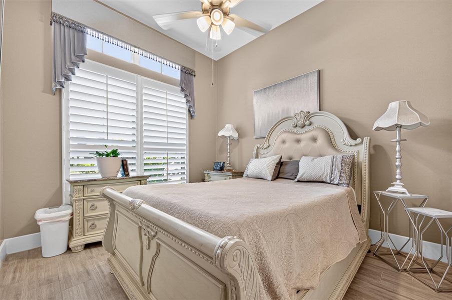 This cozy bedroom features elegant furniture with a vintage touch, a soft color palette, and ample natural light from large windows with shutters. The ceiling fan adds comfort, while stylish lamps and decor complete the inviting atmosphere. This cozy bedroom features elegant furniture with a vintage touch, a soft color palette, and ample natural light from large windows with shutters. The ceiling fan adds comfort, while stylish lamps and decor complete the inviting atmosphere.