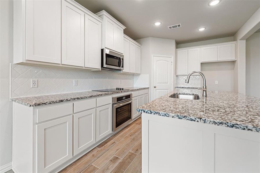 Kitchen featuring light stone countertops, decorative backsplash, recessed lighting, wood tiled floors, and white cabinets Kitchen featuring light stone countertops, decorative backsplash, recessed lighting, wood tiled floors, and white cabinets