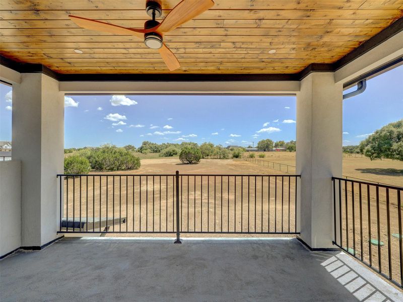 Concrete balcony with wood paneled ceiling overlooks rolling countryside fields under open skies.